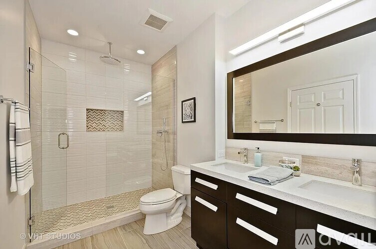 A modern bathroom with a walk-in shower, toilet, and double sinks.