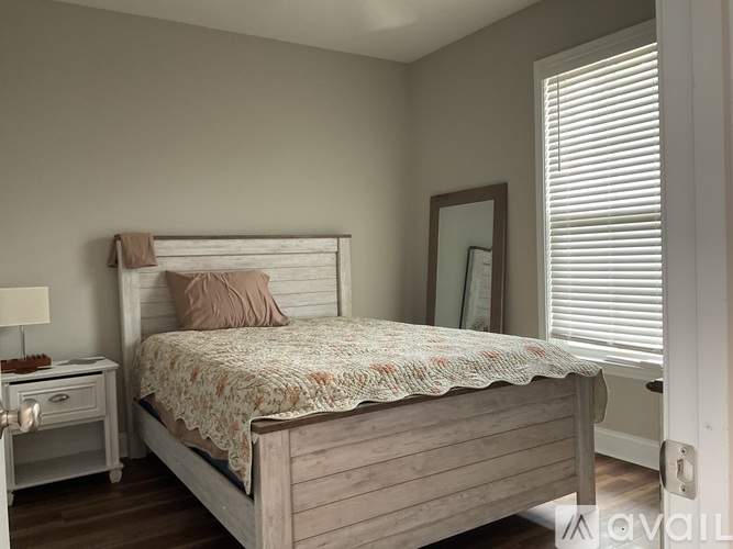 A bedroom with a bed, nightstand, and window with blinds.