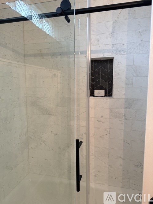 A bathroom with a glass shower door and a marble wall.