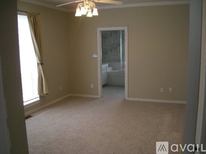 A room with beige walls and carpeting, a window with curtains, and a door leading to another room.