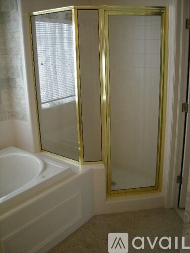 A bathroom with a white tub and gold framed shower door.