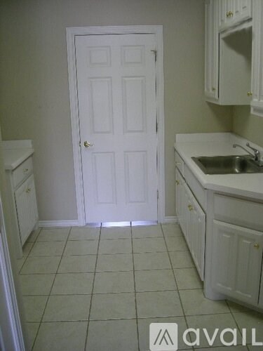 A white door is in a kitchen with white cabinets and a white sink.