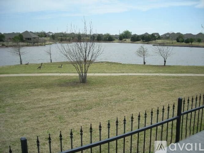 A black fence surrounds a grassy area with a lake and trees in the background.