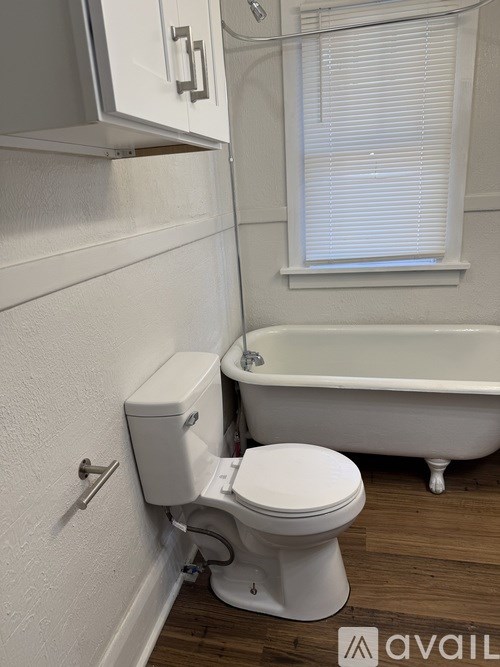 A white toilet is installed in a bathroom with a white tub and a window.