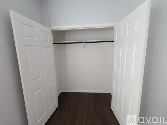 A white closet with a wooden floor and a hanging rail.
