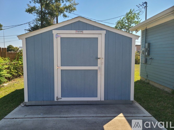 A blue shed with a white door and windows is situated in a backyard.