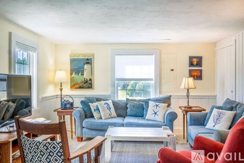 A living room with a blue couch and a painting of a lighthouse on the wall.