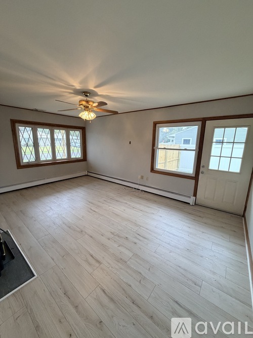 A room with a ceiling fan and light, hardwood floors, and two windows.