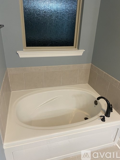 A white bathtub with a black faucet is in a bathroom with a window above it.