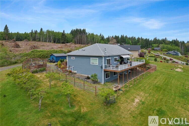 A house with a grey roof and a blue door is surrounded by a grassy area and trees.