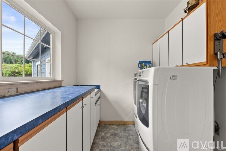 A white washing machine sits in a laundry room with a window and a blue counter.