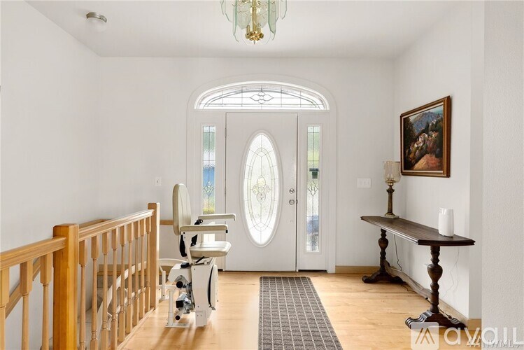 A room with a staircase, a table, a chair, and a painting on the wall.