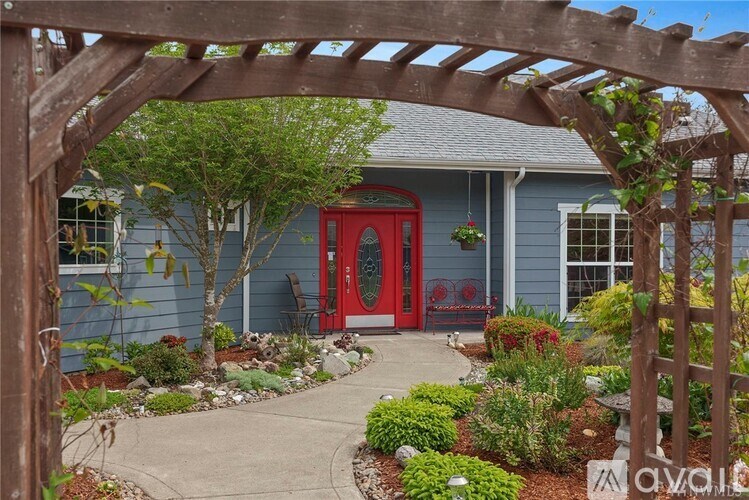 A blue house with a red door and a wooden pergola.