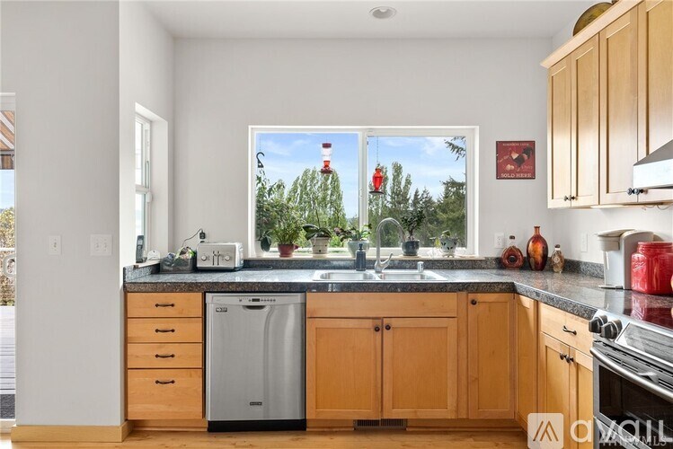 A kitchen with wooden cabinets and a large window overlooking a forest.