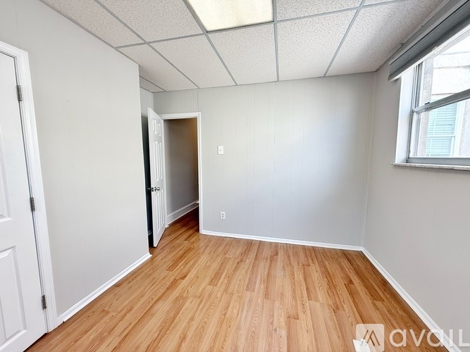 A room with wooden flooring and white walls, with a doorway leading to another room.