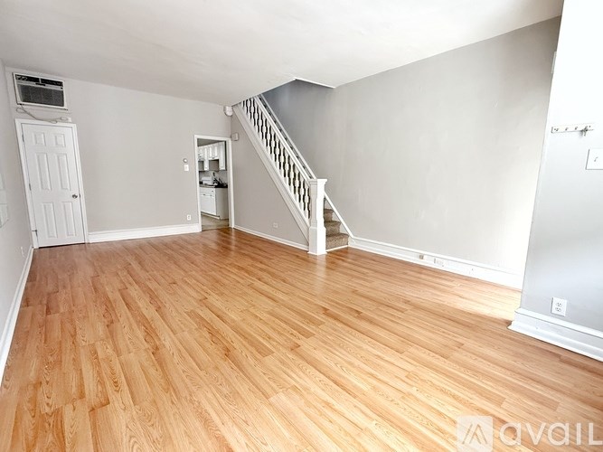 A room with wooden flooring and a staircase leading to another room.