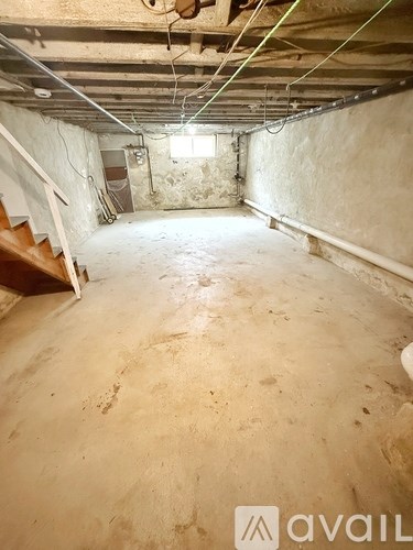 A spacious basement with a staircase and exposed pipes.