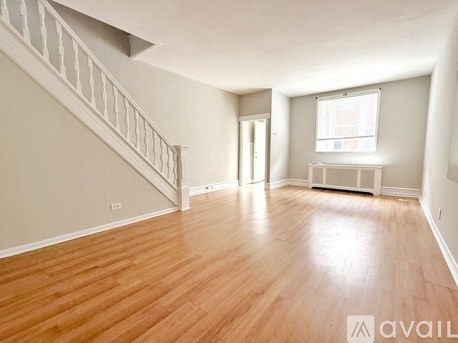 A spacious room with wooden flooring and a staircase on the left side.