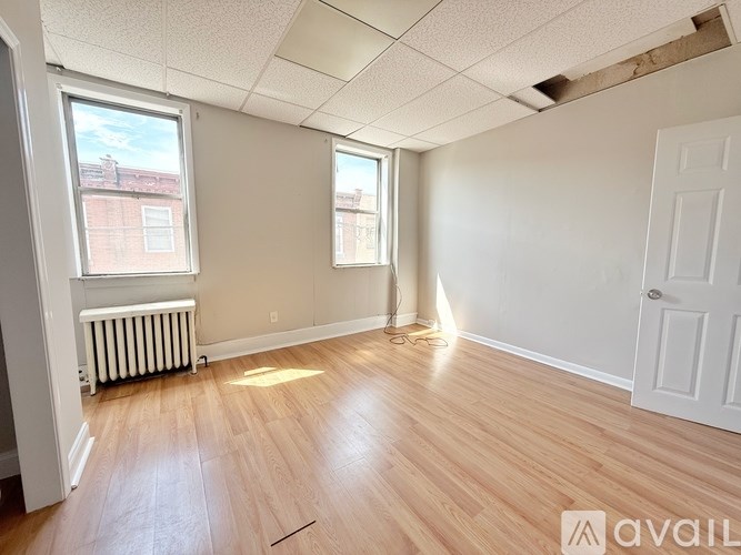 A room with wooden floors and white walls, with a window and a door visible.