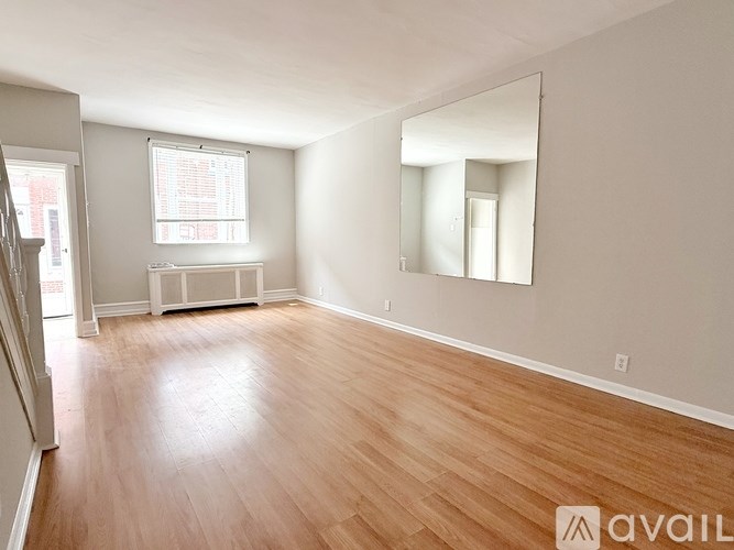 A spacious room with wooden flooring and a large mirror on the wall.