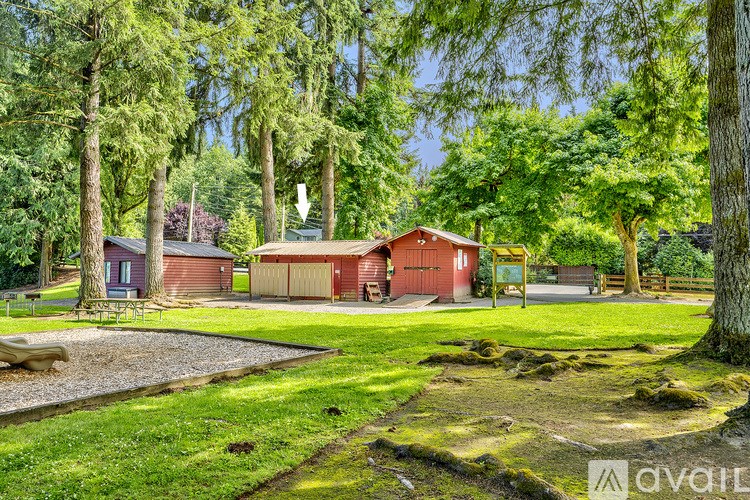 A house with a red roof is surrounded by trees and a gravel path.