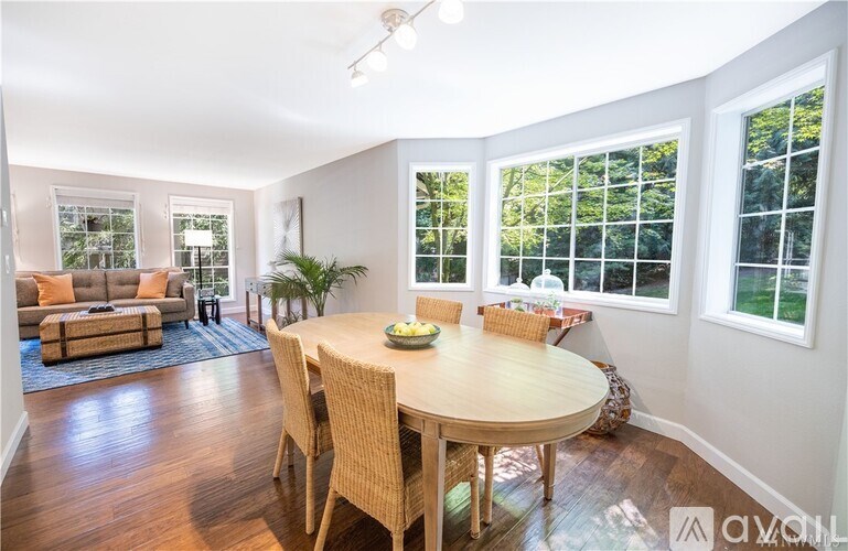 A dining room with a round table and chairs with a view of trees outside the windows.