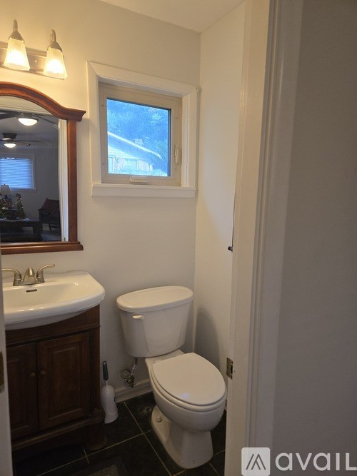 A white toilet in a bathroom with a window above it.