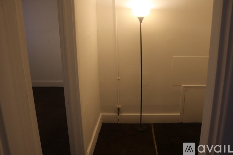 A lamp with a white shade is on in a dimly lit room.