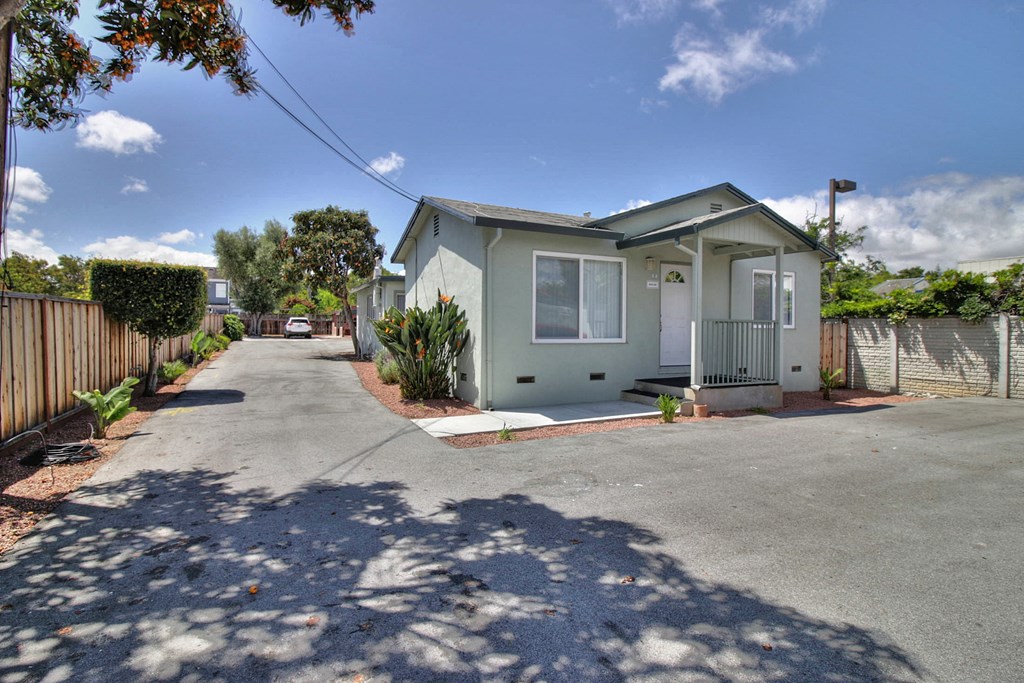 A house with a grey roof and white walls is surrounded by a fence and has a driveway in front.