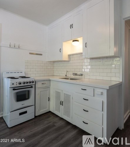A white kitchen with a stove, sink, and cabinets.