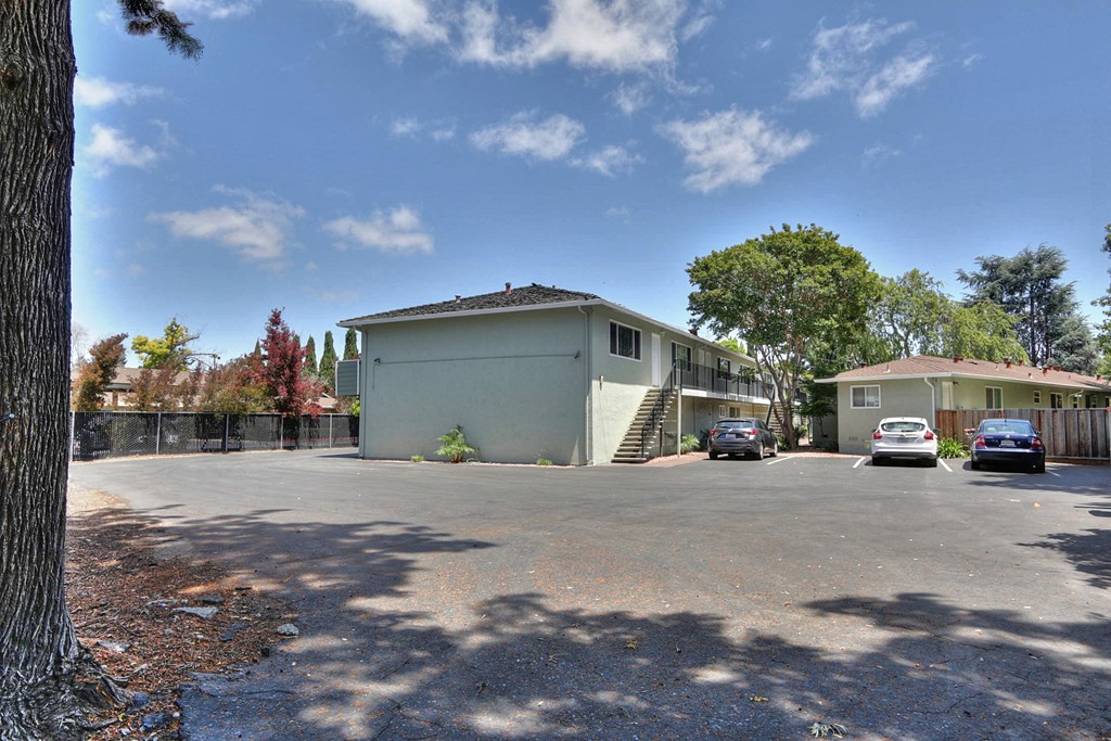 A large white building with a grey roof is surrounded by a parking lot.