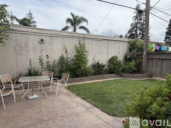 A patio with a table and chairs is surrounded by a green lawn and a wall.
