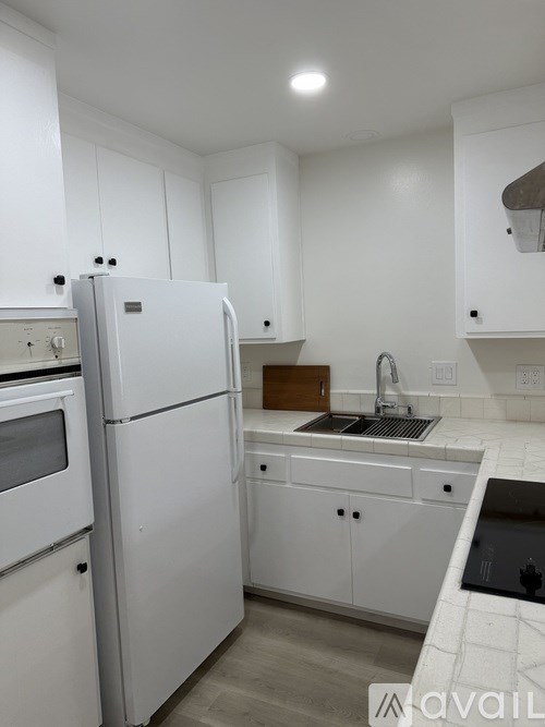 A white kitchen with a refrigerator, sink, and cabinets.