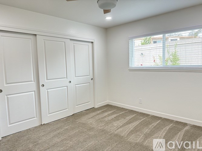 A room with a carpeted floor, two doors, and a window with blinds.