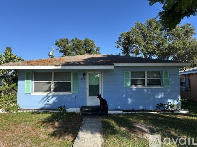 A blue house with a brown roof and a black dog sitting in front.