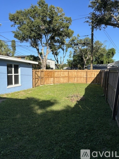 A backyard with a blue house, a wooden fence, and a tree.