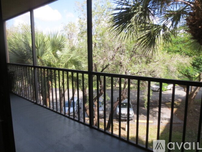 A balcony with a black railing overlooks a street with cars and trees.