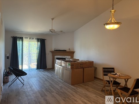 A living room with a dining table and chairs, a ceiling fan, and a window with curtains.