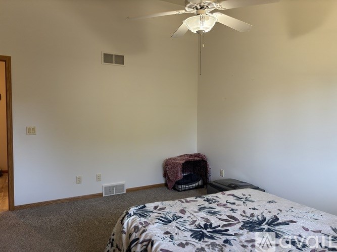 A bedroom with a bed, a ceiling fan, and a dog crate.