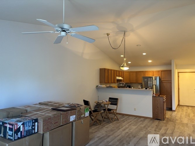 A room with a ceiling fan and a kitchen area with a refrigerator, sink and cabinets.