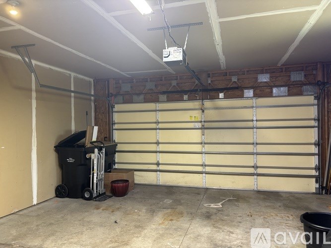 A room with a white ceiling and a large white door with a garage door opener hanging from the ceiling.