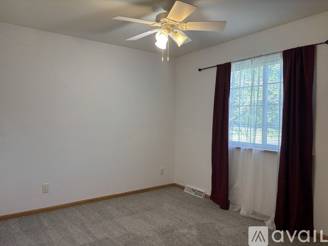 A room with a ceiling fan and a window with curtains.