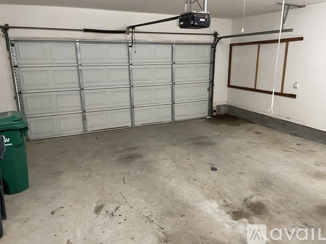 A large garage with a closed white door and a green trash can.