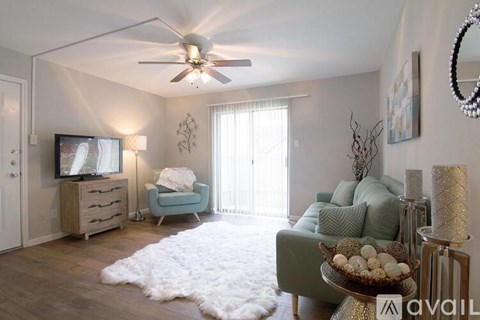A living room with a white rug, a green couch, a wooden dresser, a television, and a ceiling fan.