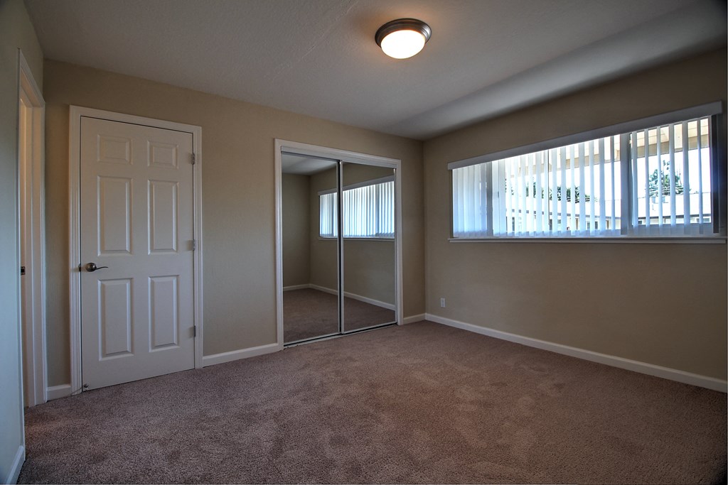 an empty living room with a mirrored closet and a window