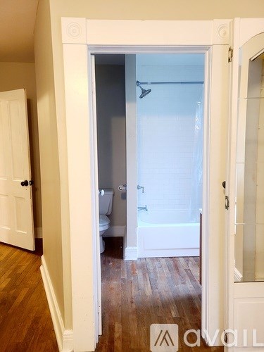A white door is open to a bathroom with a toilet and a shower.