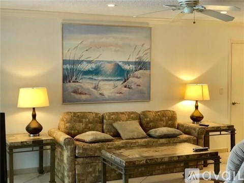 A living room with a couch, two lamps, and a painting of a beach scene.