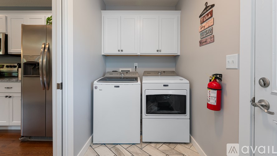 A kitchen with white appliances and cabinets, a fire extinguisher on the wall, and a doorway leading to another room.