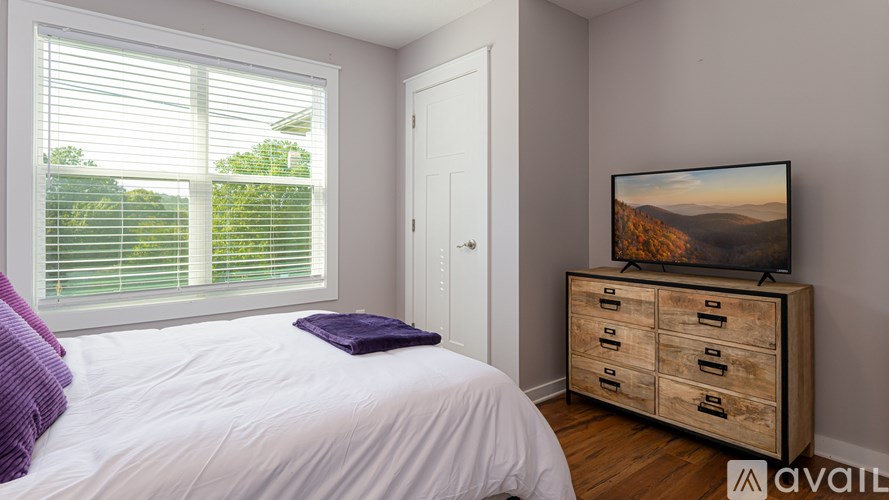 A bedroom with a bed, a dresser, and a window with blinds.