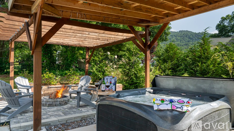 A hot tub is surrounded by chairs and a fire pit under a wooden pergola.